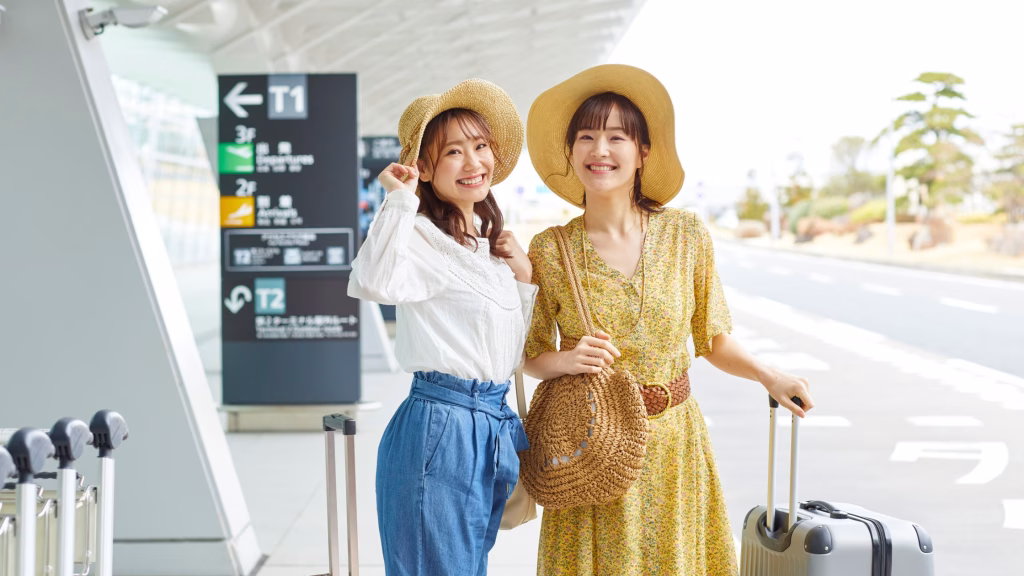 two female asian travellers outside the airport with their lugggage and smiling